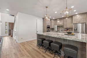 Kitchen featuring light stone countertops, stainless steel refrigerator with ice dispenser, a kitchen bar, a chandelier, and backsplash