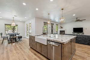 Kitchen featuring stainless steel dishwasher, open floor plan, a textured ceiling, ceiling fan, and a center island with sink