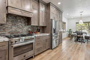 Kitchen featuring high end appliances, light wood-style floors, a textured ceiling, light stone counters, and hanging light fixtures
