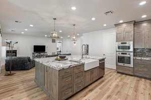 Kitchen featuring light stone counters, open floor plan, a center island with sink, and light wood-type flooring