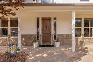 View of exterior entry with covered porch, stone siding, and stucco siding