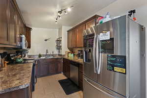Kitchen with dark countertops, stainless steel appliances, light tile patterned floors, and dark wood finish cabinets