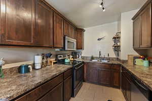 Kitchen with stainless steel appliances, dark countertops, and dark wood finish cabinetry