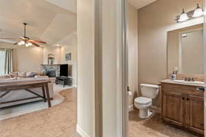 Half bath with vanity, a ceiling fan, a fireplace, vaulted ceiling, and light tile patterned floors