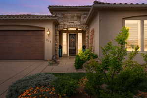 View of exterior entry with stucco siding, stone siding, an attached garage, and driveway