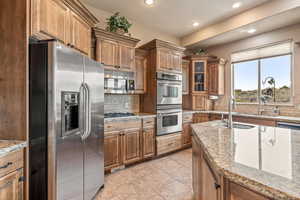 Kitchen featuring stainless steel appliances, glass fronted cabinets, wood finish cabinetry, light tile patterned floors, and backsplash