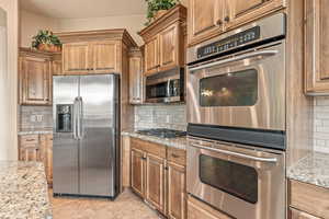 Kitchen featuring stainless steel appliances, light stone countertops, backsplash, and wood finish cabinets