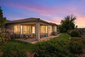 Back of property at dusk with a lawn, stucco siding, a patio, and a tile roof