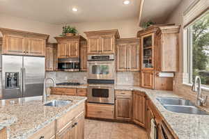 Kitchen with stainless steel appliances, light stone countertops, glass insert cabinets, healthy amount of natural light, and recessed lighting