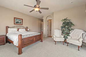 Bedroom with light colored carpet, ceiling fan, and arched walkways