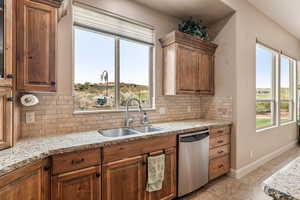 Kitchen featuring light stone countertops, dishwasher, tasteful backsplash, and wood finish cabinets