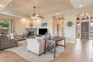 Living area featuring a tray ceiling, ceiling fan, hanging lights, light tile patterned floors, and a fireplace
