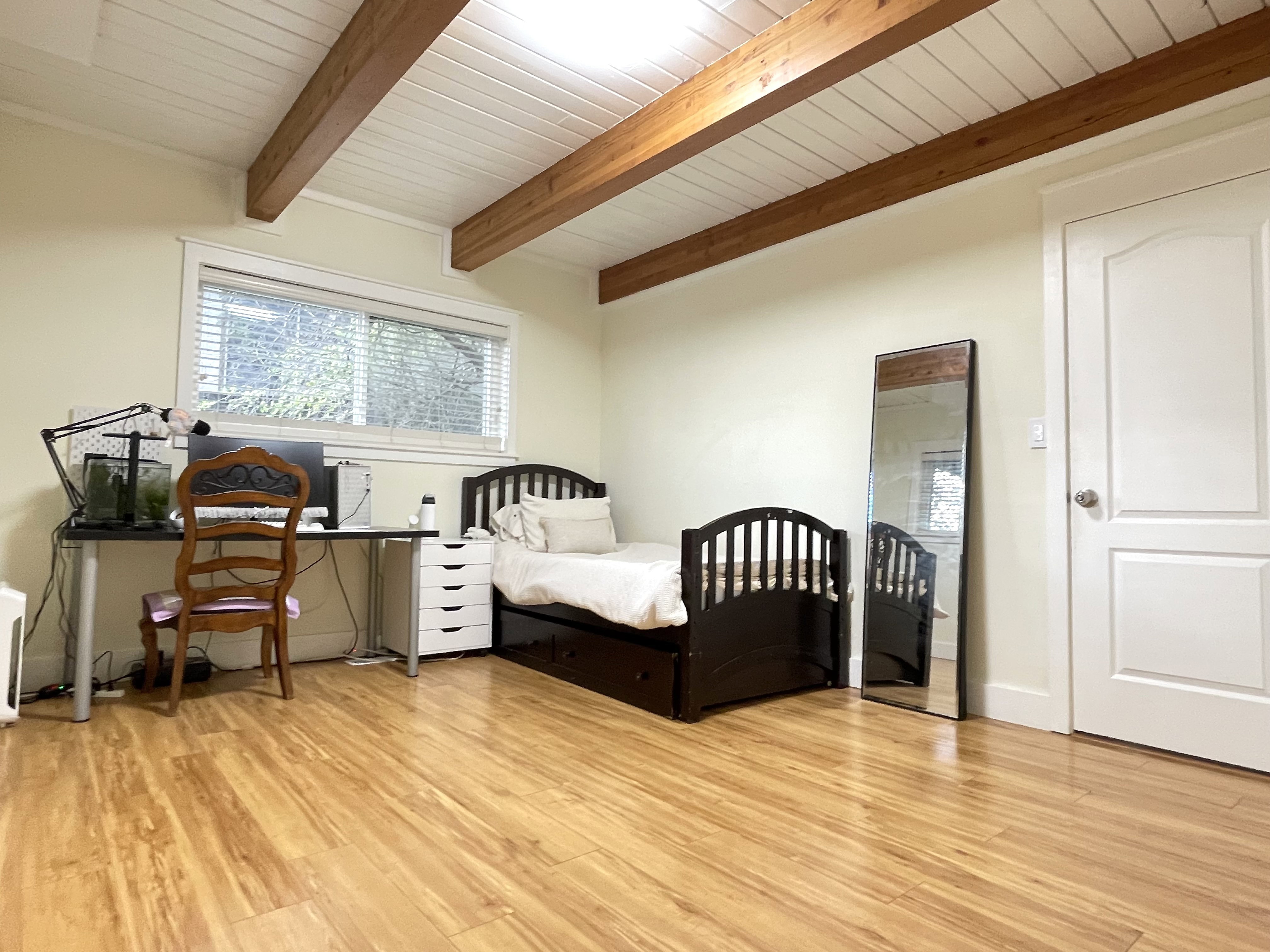 Bedroom featuring light wood-type flooring, an office area, and a wooden ceiling with exposed beams