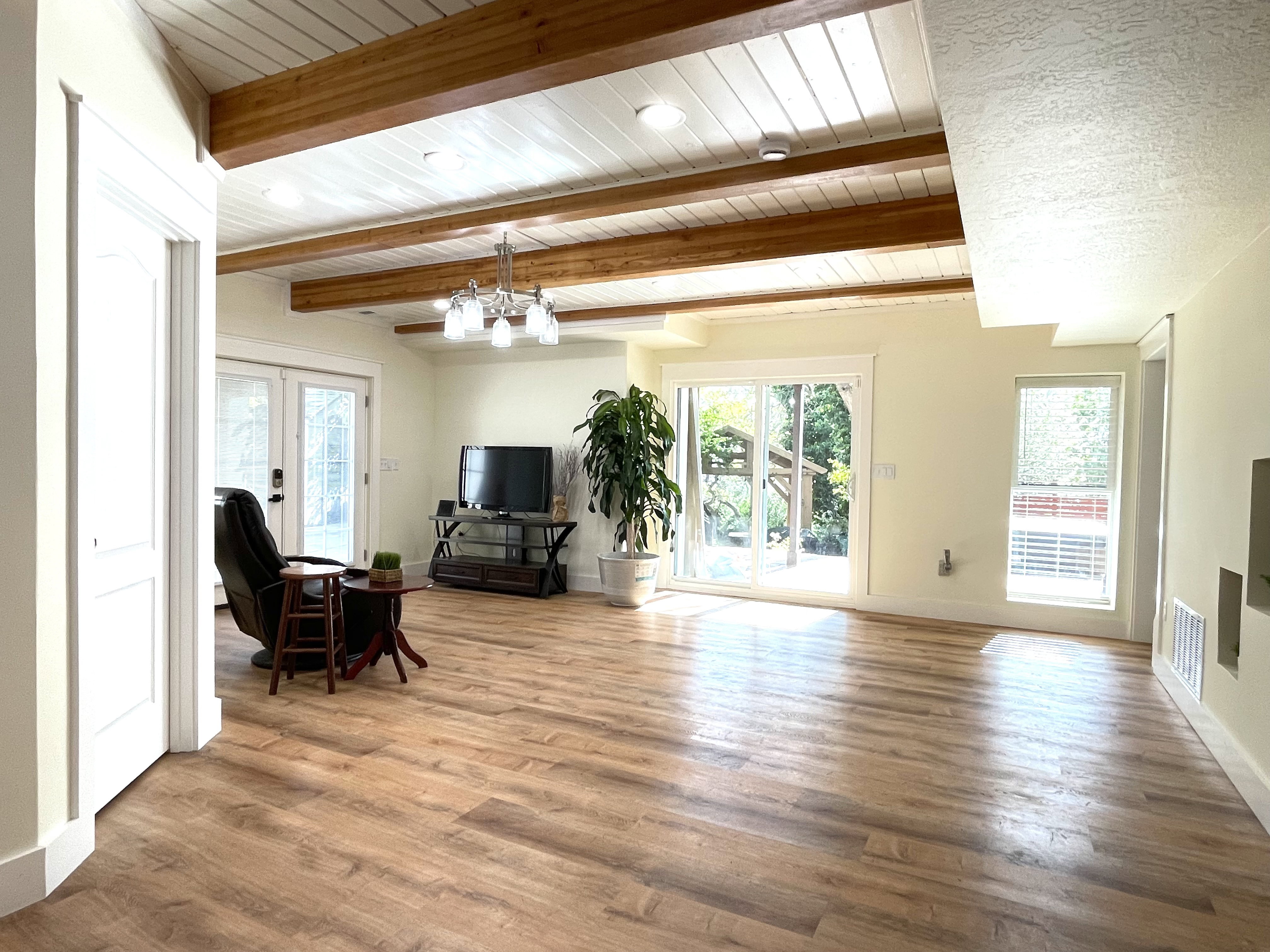 Living area with french doors, beam ceiling, light wood finished floors, and hanging lights