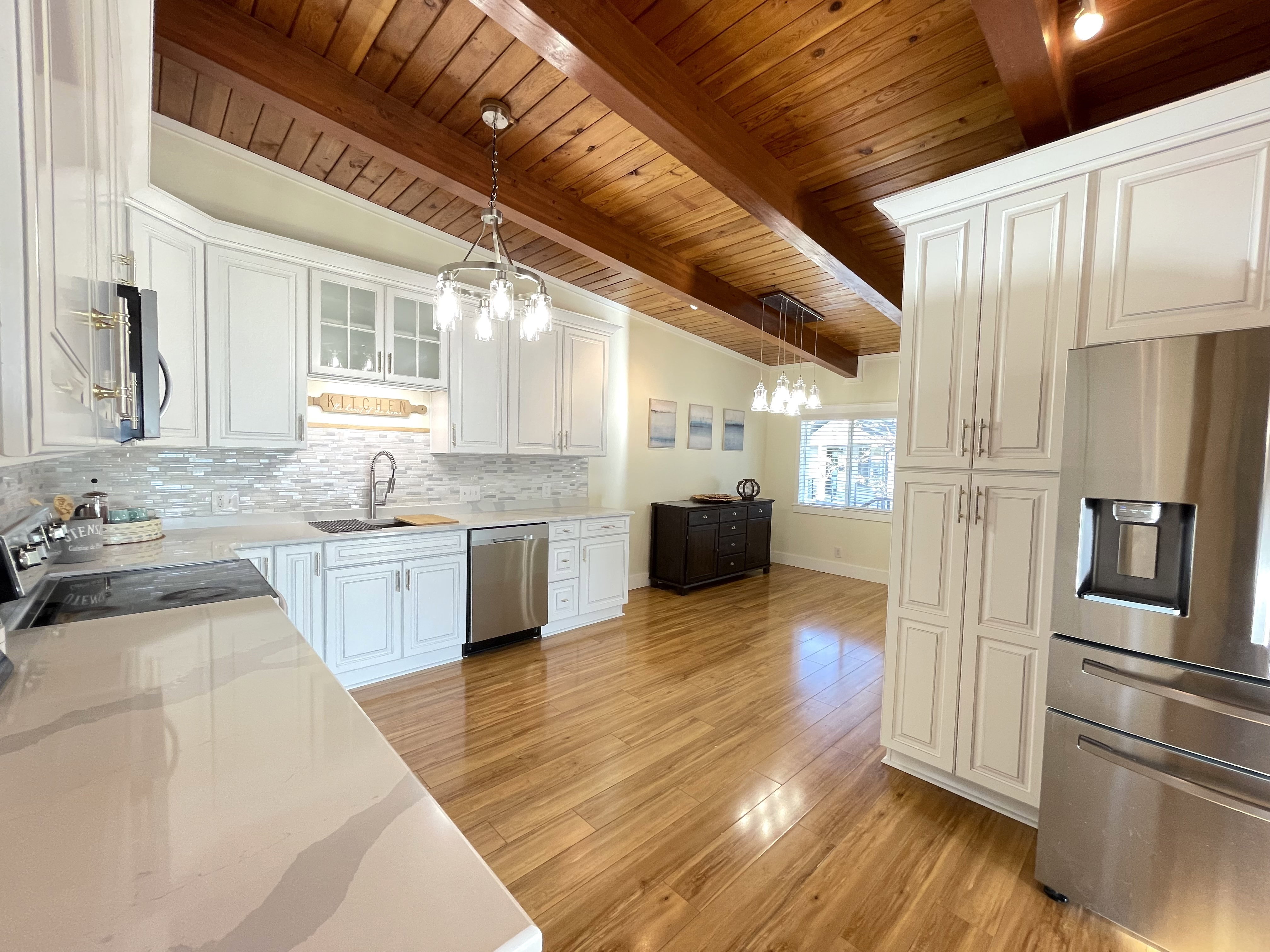 Kitchen featuring stainless steel appliances, light wood-type flooring, decorative backsplash, white cabinetry, and suspended lighting