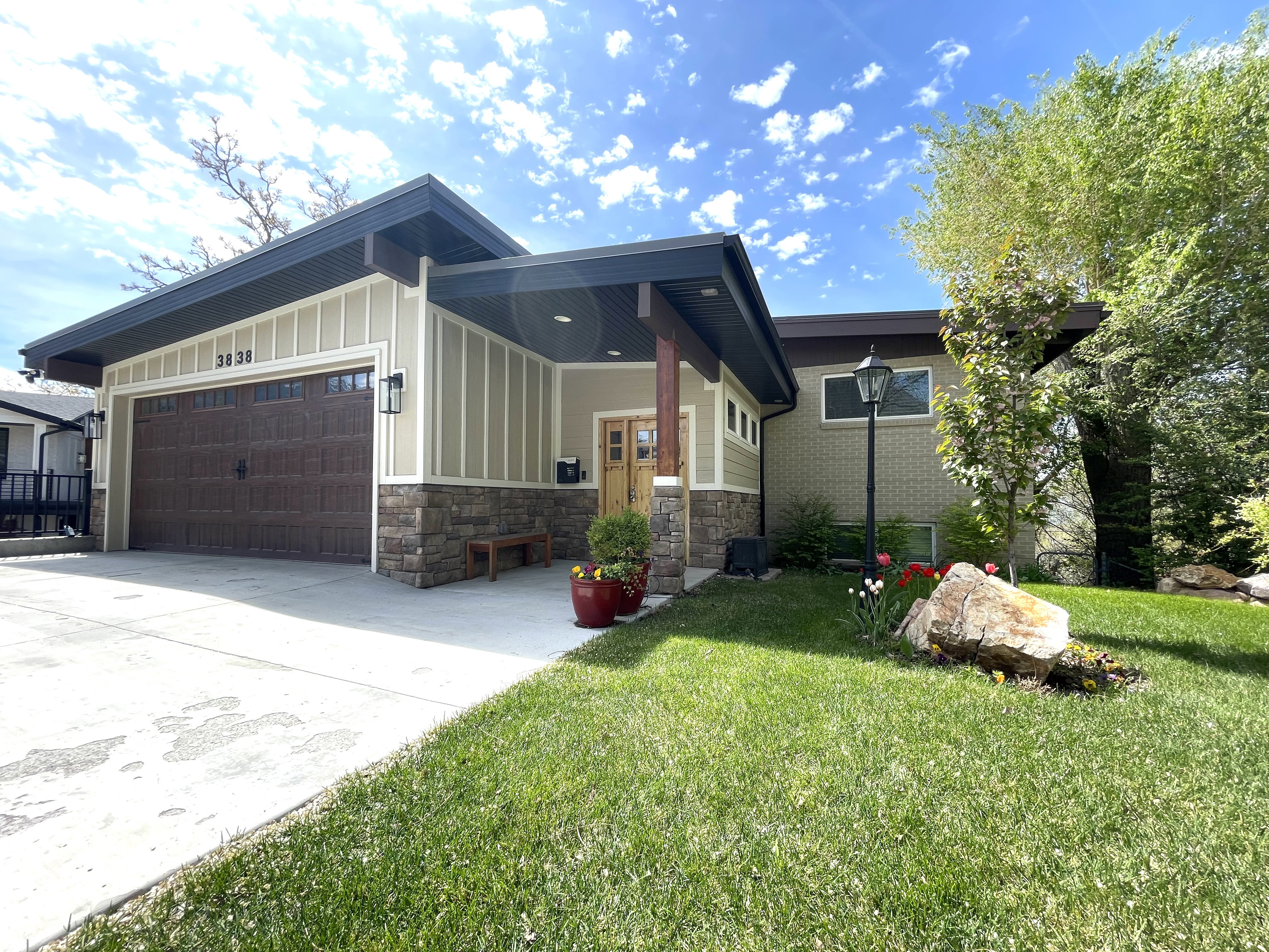 View of front facade featuring an attached garage, concrete driveway, stone siding, a front yard, and board and batten siding