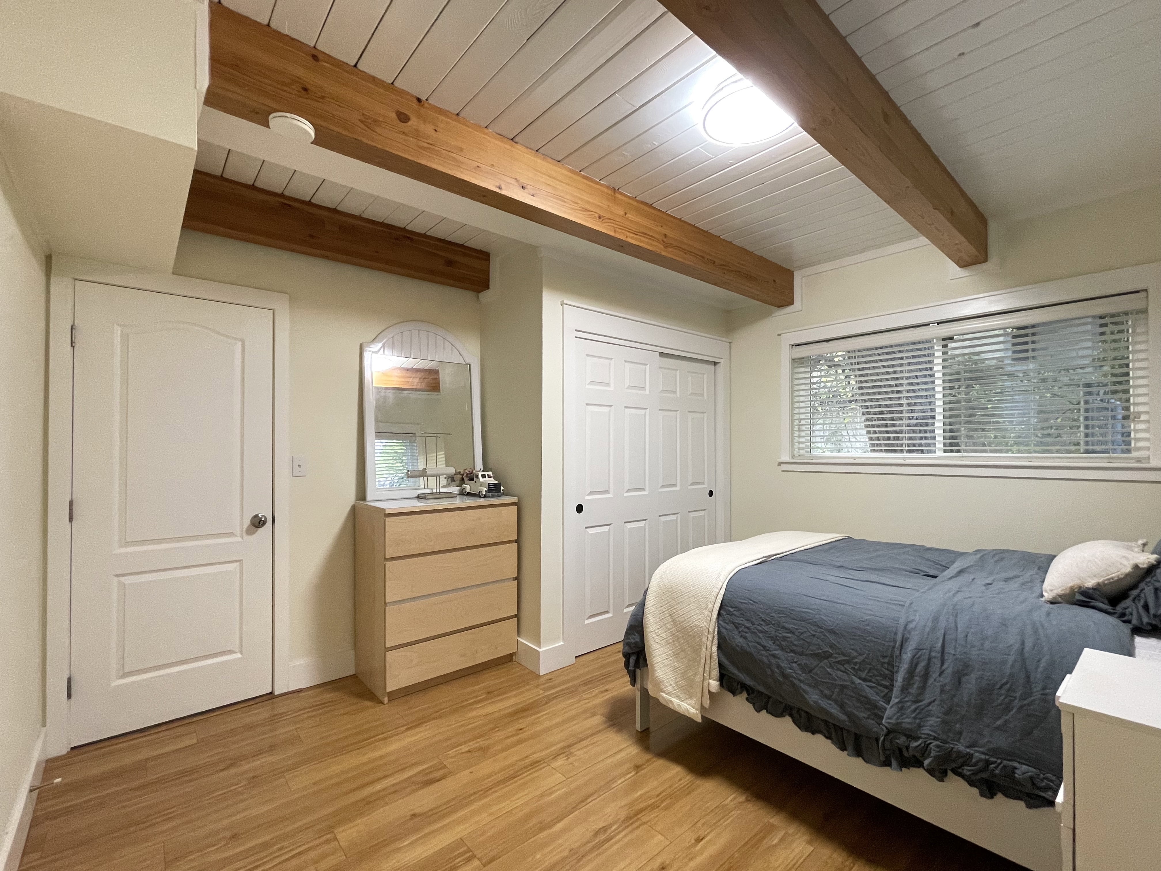Bedroom with light wood-type flooring, a wooden ceiling with exposed beams, and a closet