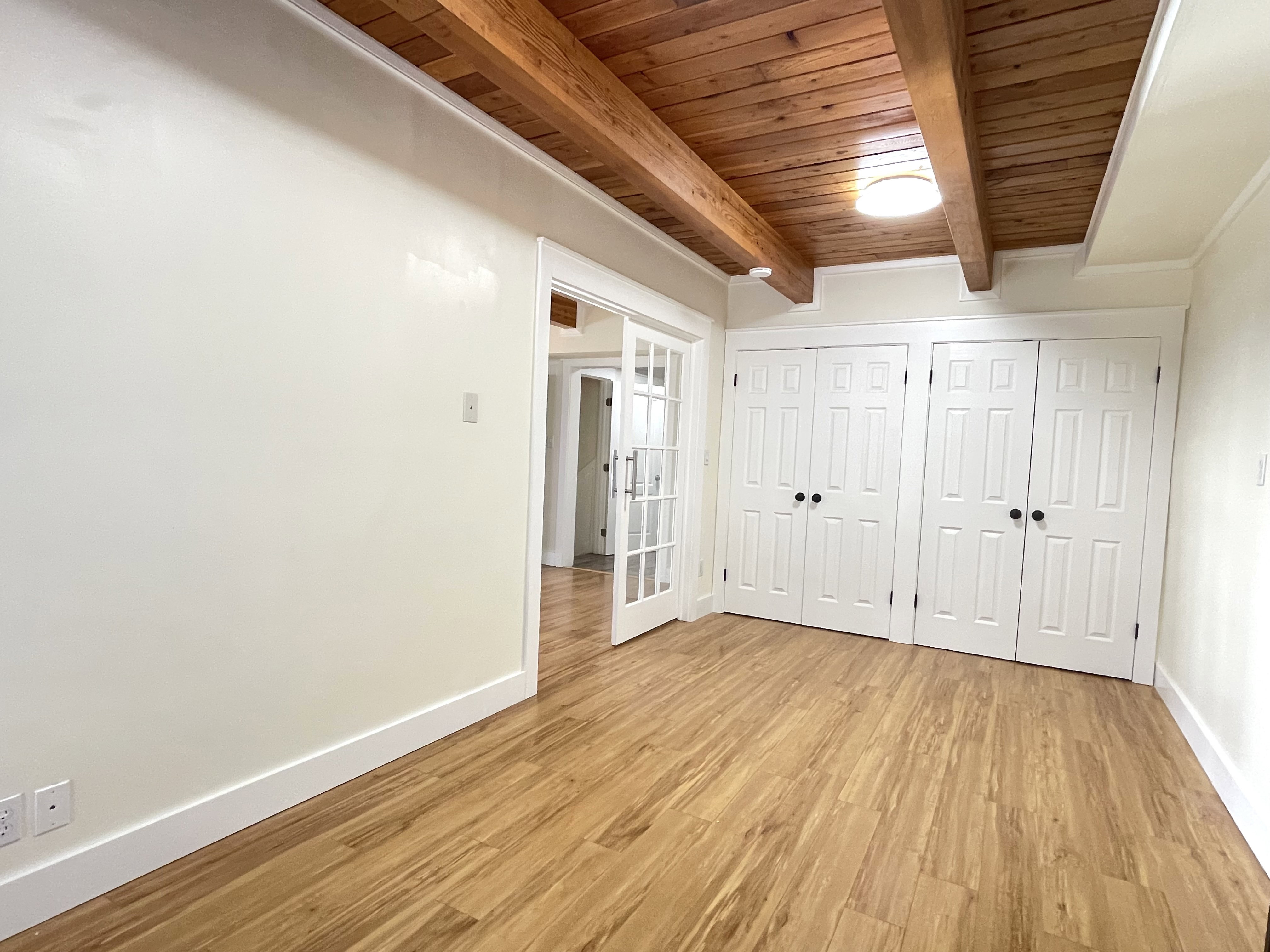 Unfurnished bedroom with multiple closets, light wood finished floors, and a wood ceiling with exposed beams