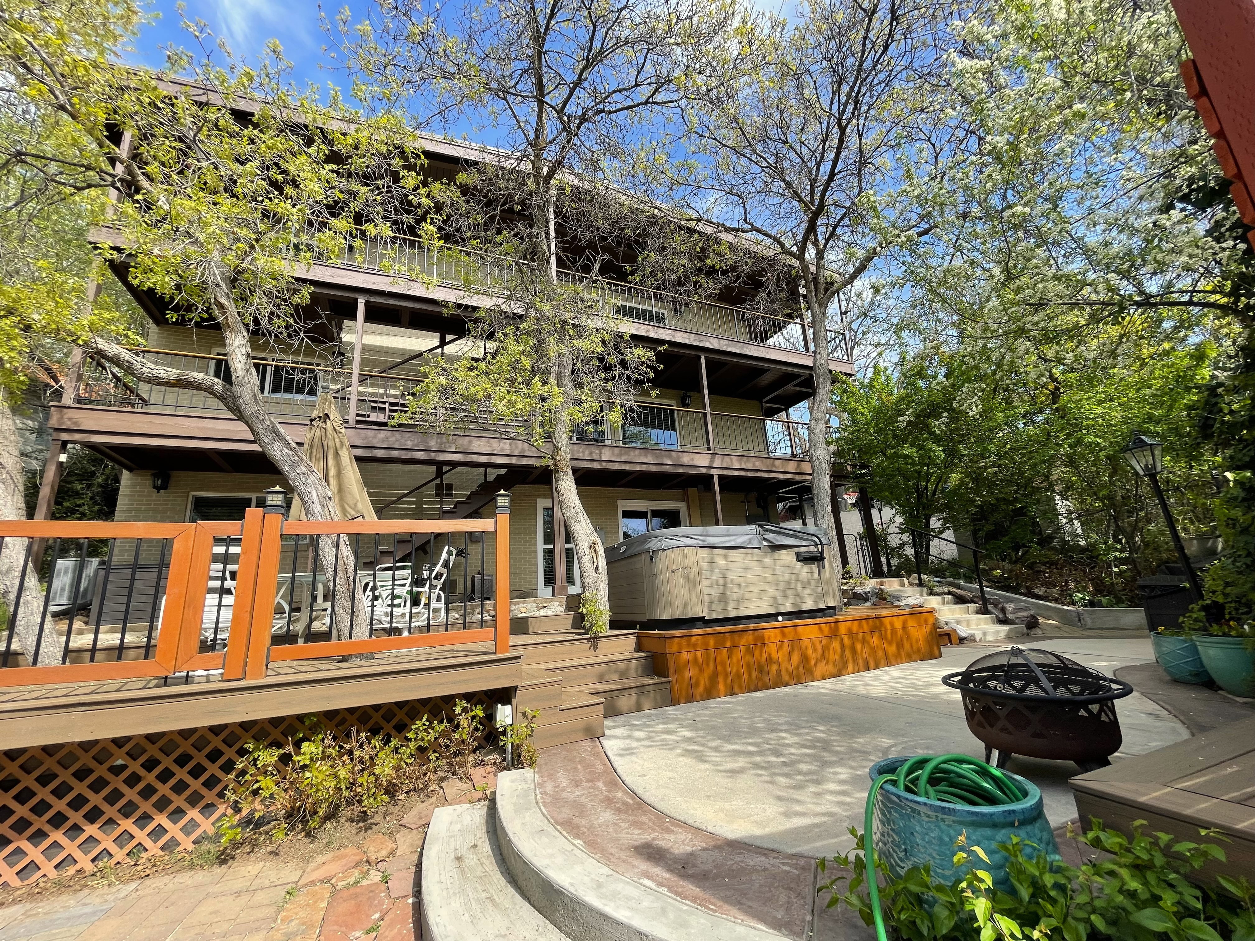Back of property with an outdoor fire pit, a balcony, a patio area, a hot tub, and a deck
