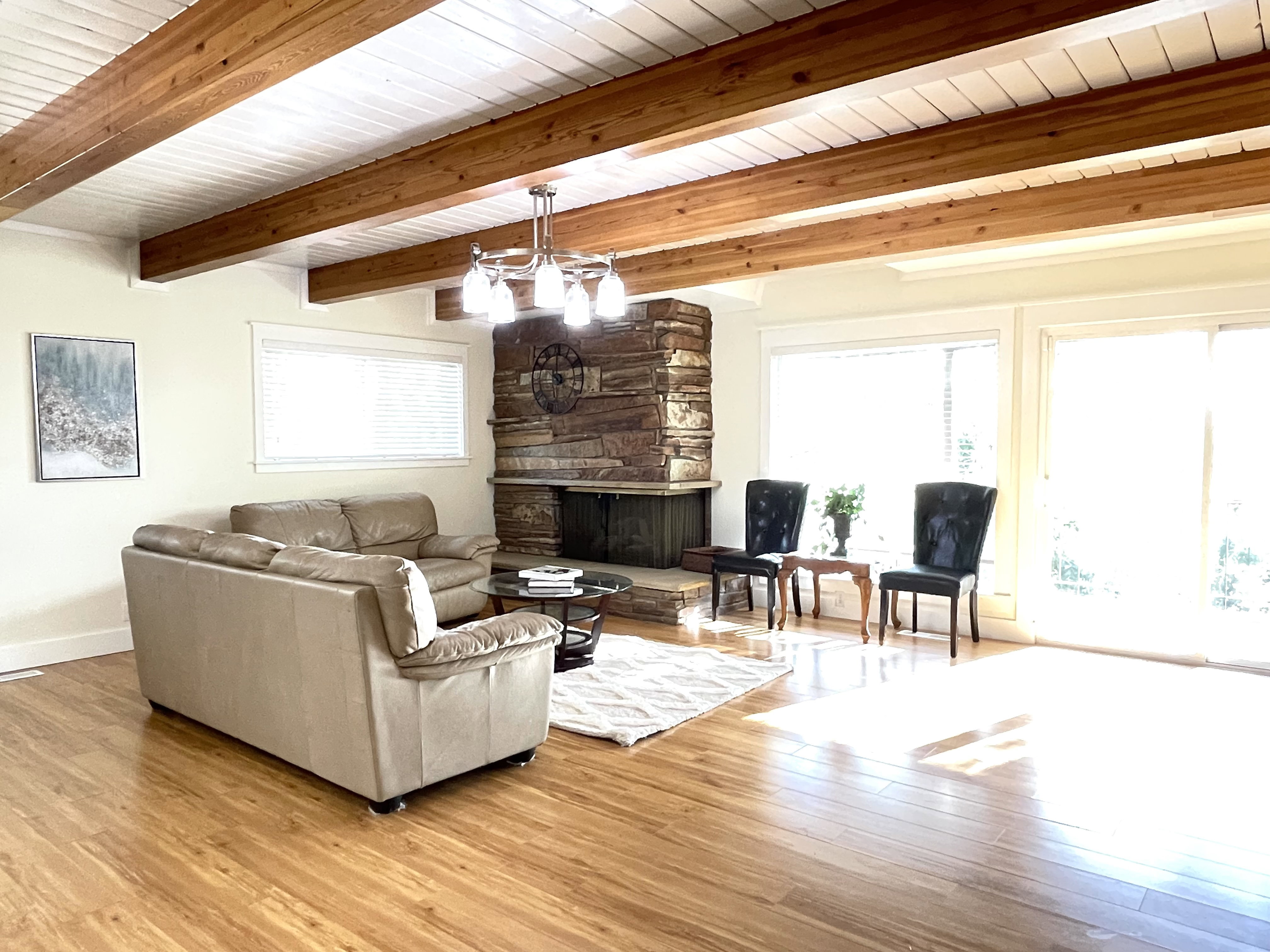 Living room featuring healthy amount of natural light, light wood finished floors, a fireplace, suspended lighting, and beamed ceiling