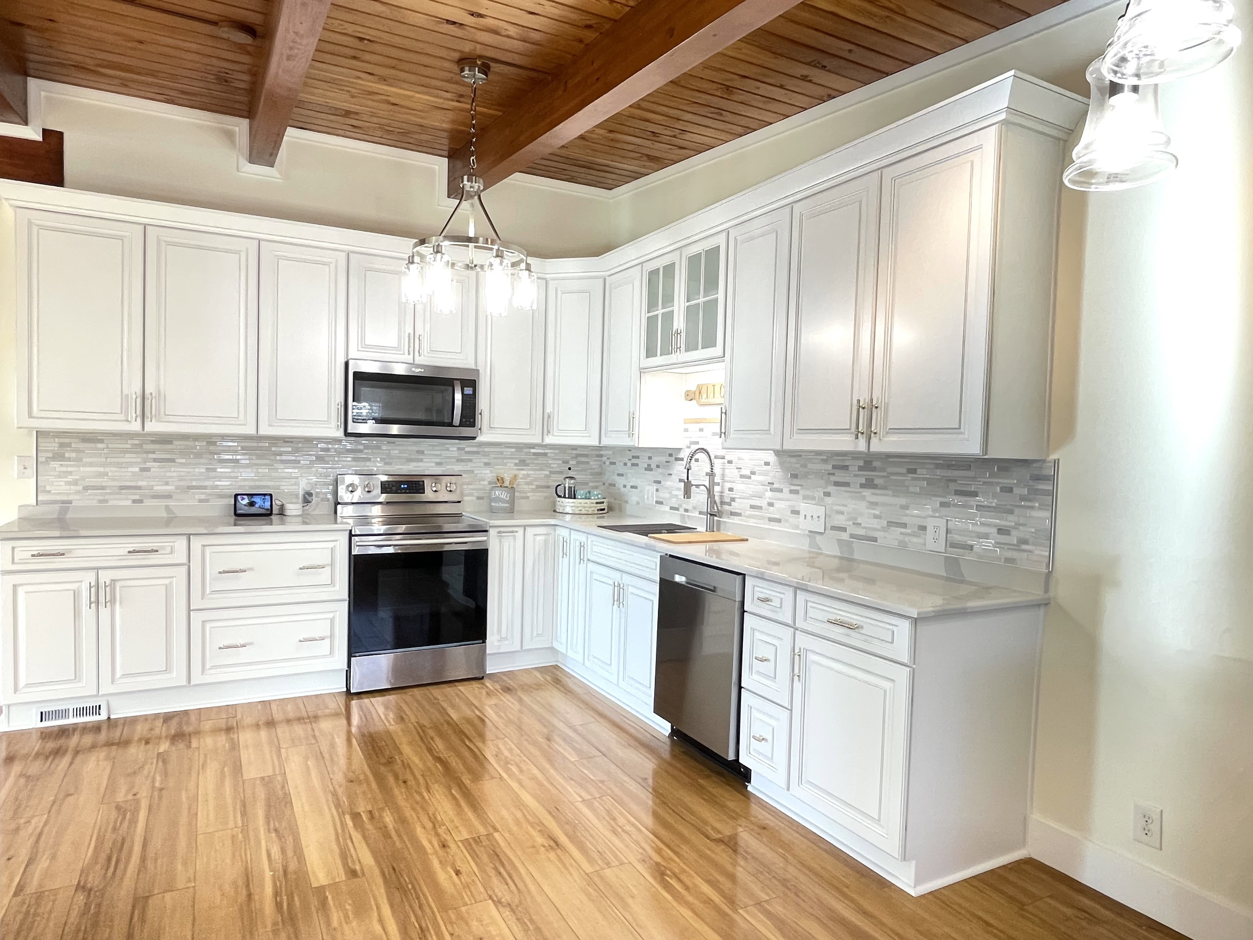 Kitchen featuring stainless steel appliances, glass insert cabinets, white cabinetry, tasteful backsplash, and light wood-style floors