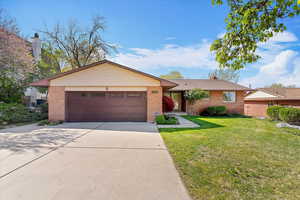 Single story home featuring a front yard, driveway, an attached garage, and brick siding