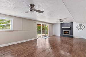 Unfurnished living room featuring a brick fireplace, a textured ceiling, dark wood finished floors, and ceiling fan