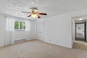 Unfurnished bedroom featuring carpet floors, a textured ceiling, a baseboard heating unit, a closet, and ceiling fan