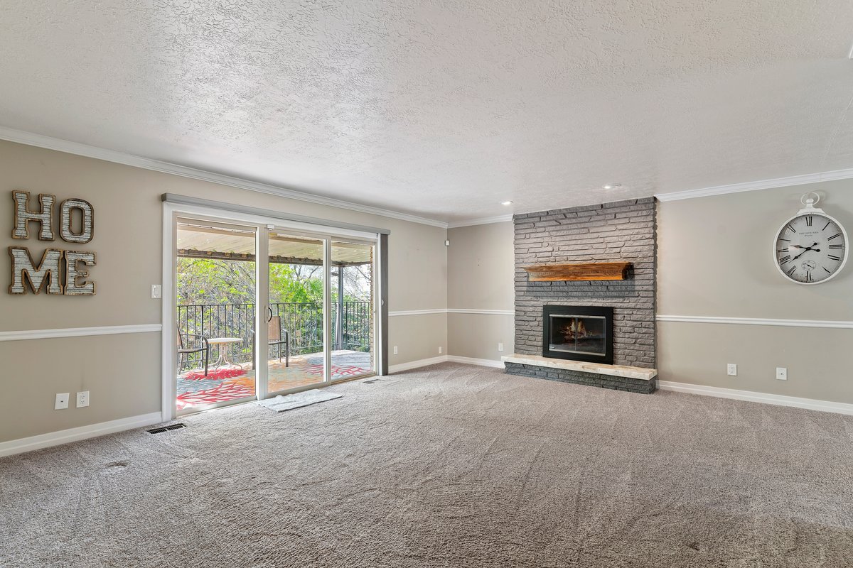 Spacious living area featuring a stone-clad fireplace with a wood mantel, a sliding glass door providing outdoor access, and neutral wall tones with white trim