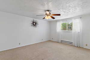Carpeted empty room featuring ceiling fan, baseboard heating, and a textured ceiling