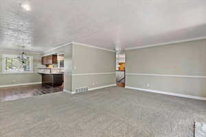 Unfurnished living room featuring a chandelier, ornamental molding, a textured ceiling, and dark colored carpet