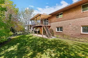Back of property featuring a patio, a yard, brick siding, and a wooden deck