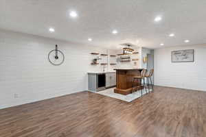 Kitchen featuring open shelves, a breakfast bar area, a textured ceiling, dark wood-style floors, and a peninsula