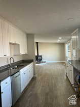 Kitchen with white cabinets, a wood stove, dark wood finished floors, stainless steel dishwasher, and dark stone counters