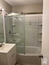 Bathroom with vanity, shower / bath combination with glass door, and a textured ceiling