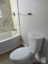 Full bathroom with washtub / shower combination and dark wood-type flooring