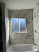 Full bath with shower / washtub combination, plenty of natural light, and a textured ceiling