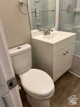 Full bath with vanity, shower / bath combination with glass door, and dark wood-style flooring