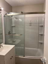 Full bath with vanity, a textured ceiling, and combined bath / shower with glass door