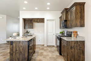 Kitchen featuring black appliances, dark wood finish cabinetry, light stone counters, and recessed lighting