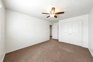 Unfurnished bedroom with dark carpet, ceiling fan, and a closet