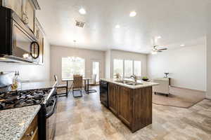 Kitchen featuring black appliances, a center island with sink, light stone countertops, a chandelier, and plenty of natural light
