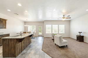 Kitchen with light stone counters, open floor plan, a kitchen island with sink, hanging lights, and dark wood finish cabinets