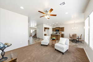 Living area featuring a ceiling fan, suspended lighting, and dark carpet