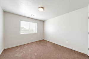 Carpeted spare room with a textured ceiling and baseboards