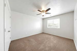 Carpeted spare room featuring a textured ceiling and ceiling fan
