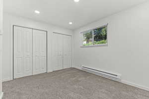 Unfurnished bedroom with a baseboard radiator, two closets, carpet flooring, and recessed lighting