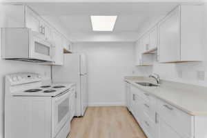 Kitchen featuring white appliances, white cabinetry, and light wood-style flooring