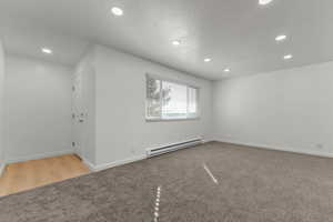 Empty room with a baseboard radiator, light colored carpet, recessed lighting, and a textured ceiling