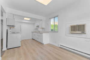 Kitchen featuring a baseboard radiator, light wood-type flooring, light countertops, white range oven, and white cabinetry
